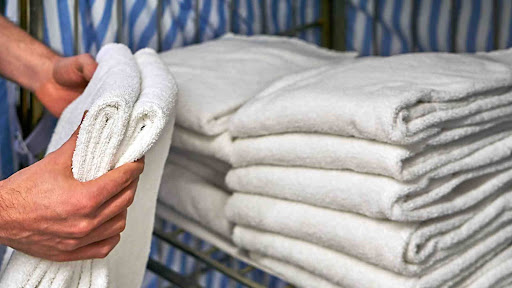 A worker in the hospitality industry chooses a towel from a folded pile that has been delivered through a same-day commercial laundry service.