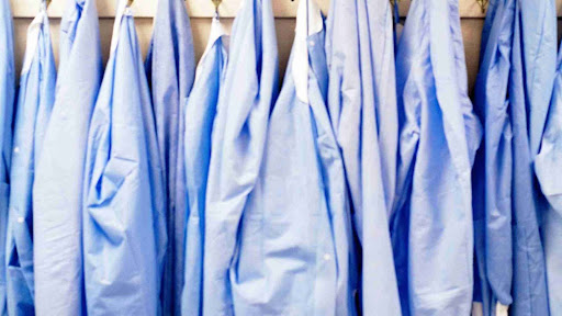 Shows a row of lab coats that are hung up in a row in a medical office after a wash from a local commercial laundry service.